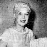 Posed photograph of a white woman with blonde hair holding sheet music